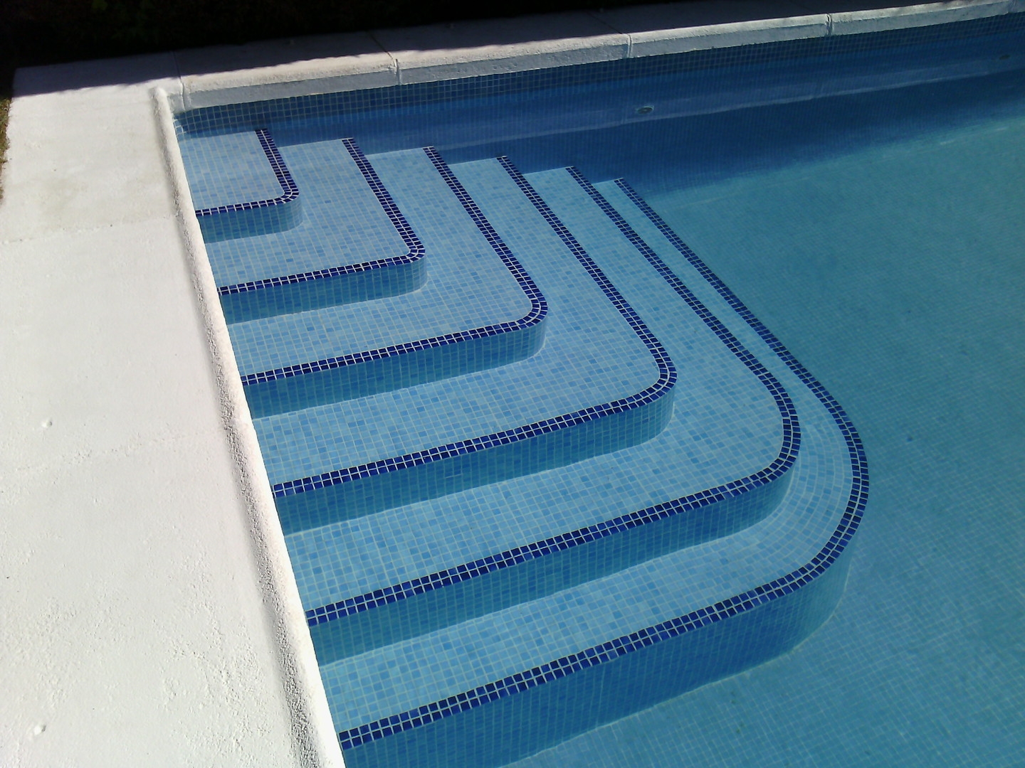A blue swimming pool with steps leading down into the water, surrounded by a clean, inviting area.
